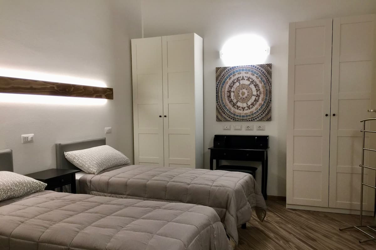 Un dormitorio con dos camas, un escritorio, un armario y una lámpara de pared.