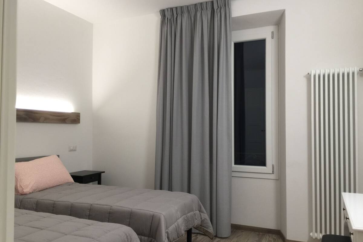 Un dormitorio con dos camas, una ventana con cortinas, un radiador y suelo de madera.