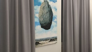 A room with a painting of a rock and waves on the wall, grey curtains, and a wooden floor. - Zannetti (Florence)