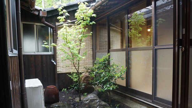 Un jardín japonés tradicional con una construcción de madera, un estanque de carpas y un farol de piedra.