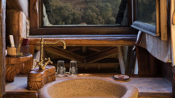 A rustic cabin interior with a large window offering a view of a forested hillside.