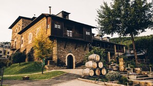 A stone building with a large arched entrance, a wooden balcony, and a garden with barrel decorations.