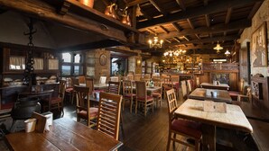 A rustic interior with wooden tables and chairs, stone walls, and a bar area with bottles and glasses.