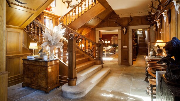 A grand staircase with wooden railings and antler decorations, leading to a dining area with a chandelier and a statue of a horse. - Pazo De Brandeso & Country Club (Arzua)