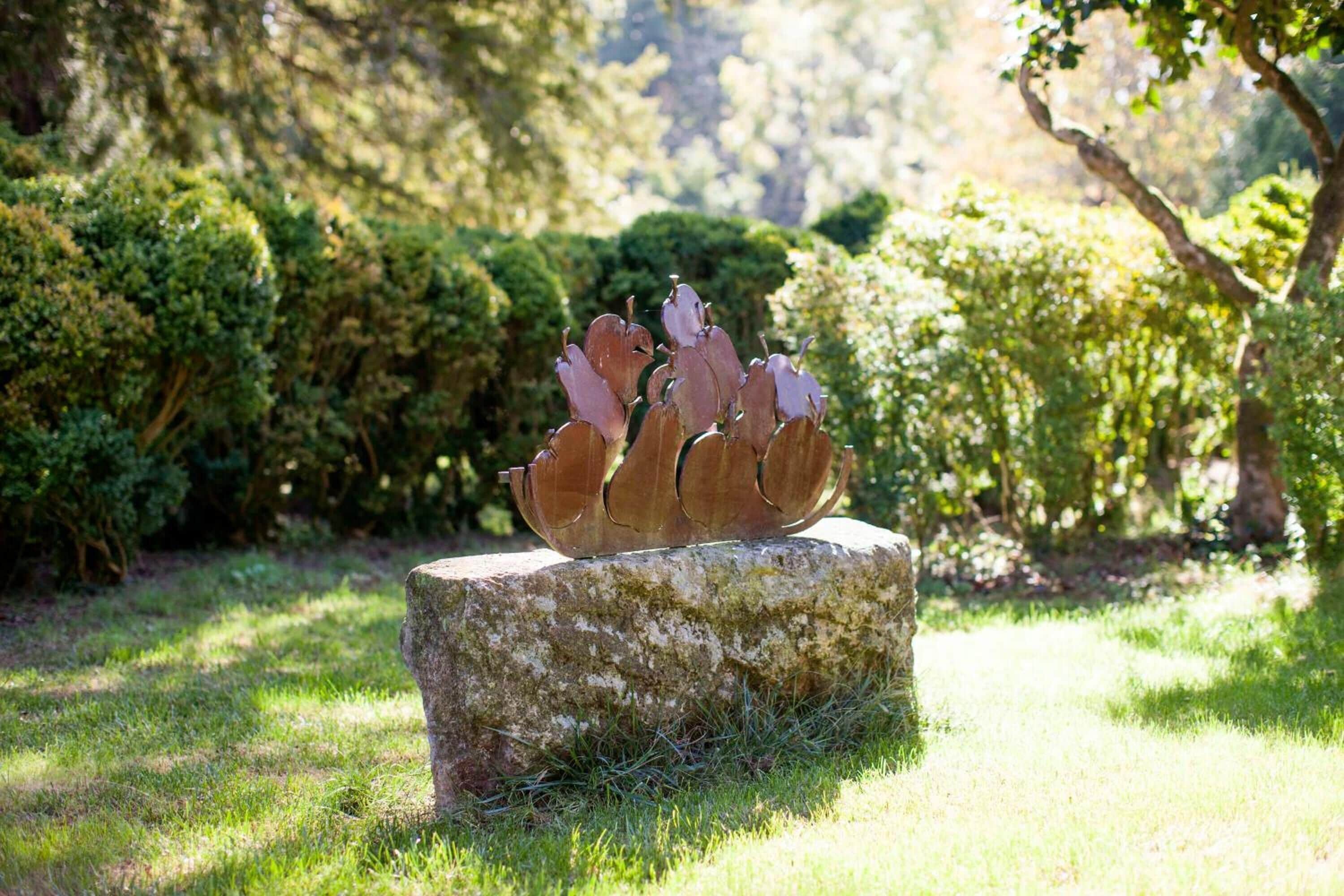 A sculpture on a stone pedestal in a garden with lush greenery and trees in the background.