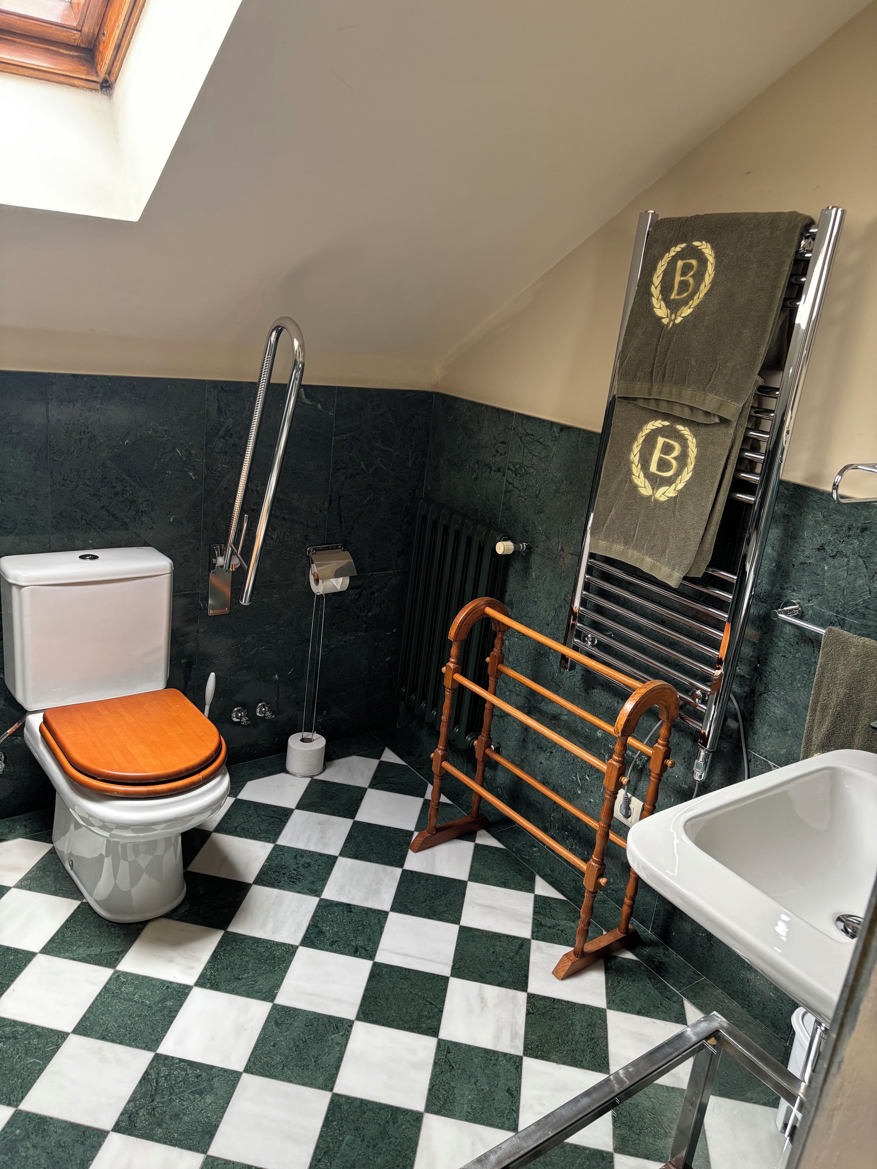 A bathroom with a checkered floor, a toilet, a bathtub, a towel rack with towels, a shower, and a radiator.