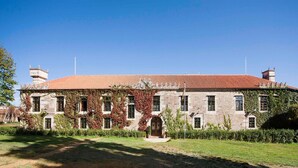 A large stone building with a red-tiled roof, surrounded by a well-maintained lawn and mature trees. - Pazo De Brandeso & Country Club (Arzua)
