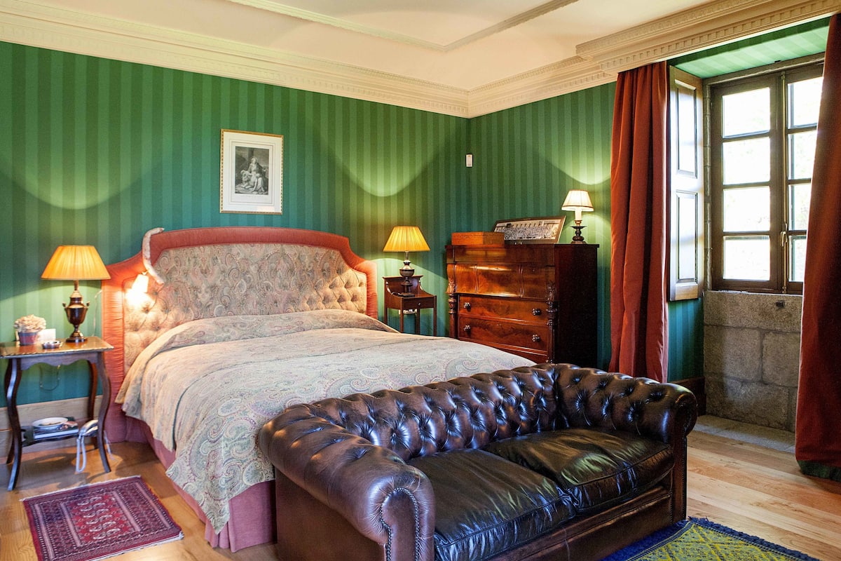 Une chambre à coucher avec un grand lit, un canapé en cuir, une commode et une fenêtre avec des rideaux.