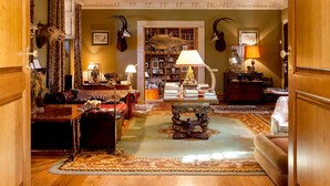 A spacious living room with a fireplace, leather furniture, a bookshelf, and mounted animal heads. - Pazo De Brandeso & Country Club (Arzua)