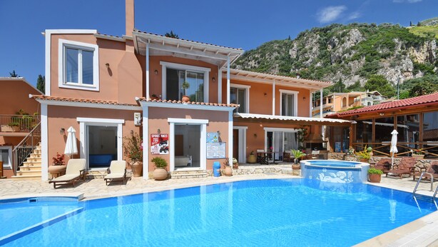 A two-story building with a swimming pool, outdoor seating, and a mountain backdrop. - Angels Pool Bar (Corfu)