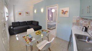 A compact living space with a kitchenette, a dining area with a table and chairs, a sofa, and a bed in the background. - Angels Pool Bar (Corfu)