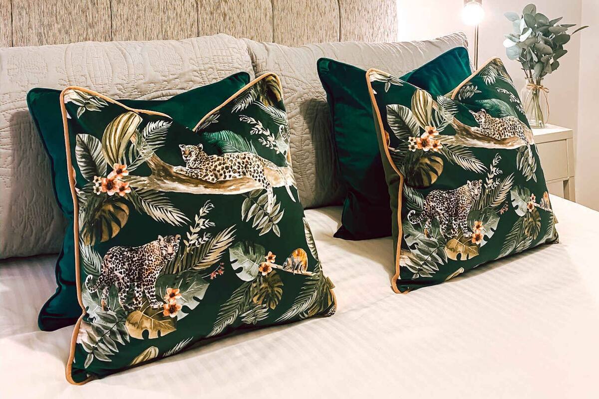 A bedroom with a tufted headboard, two green patterned pillows, and a decorative wall piece.