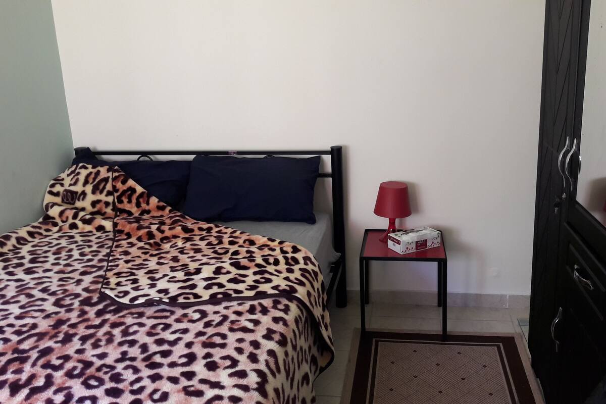 A bedroom with a bed, a nightstand, a red lamp, and a wardrobe.