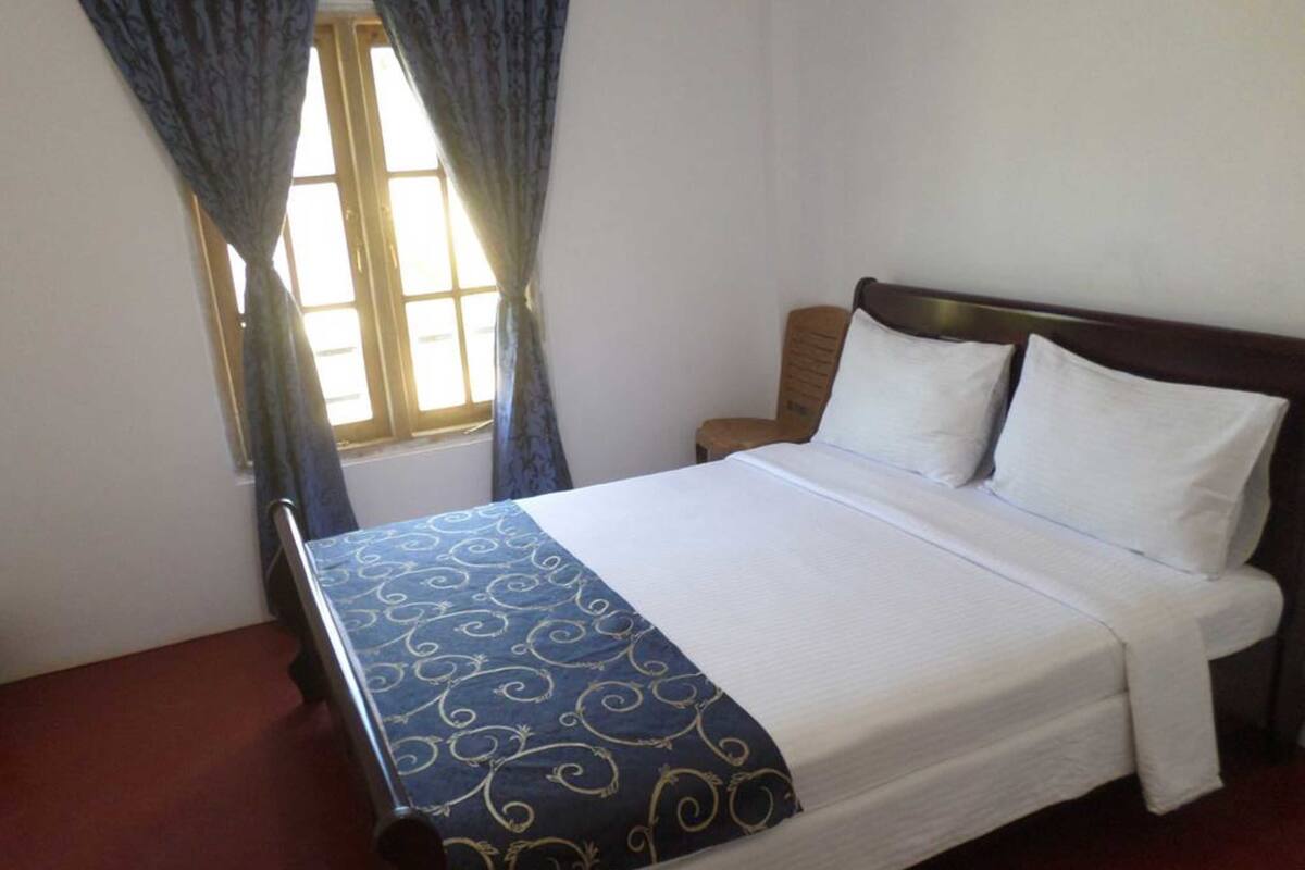 A single bed with a wooden headboard, white bedding, and a blue patterned bedspread.