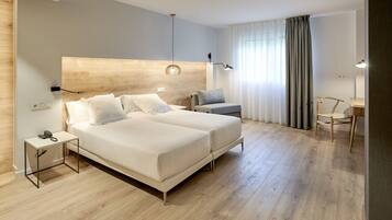 A modern hotel room with a wooden headboard, two beds, a desk, and a chair.