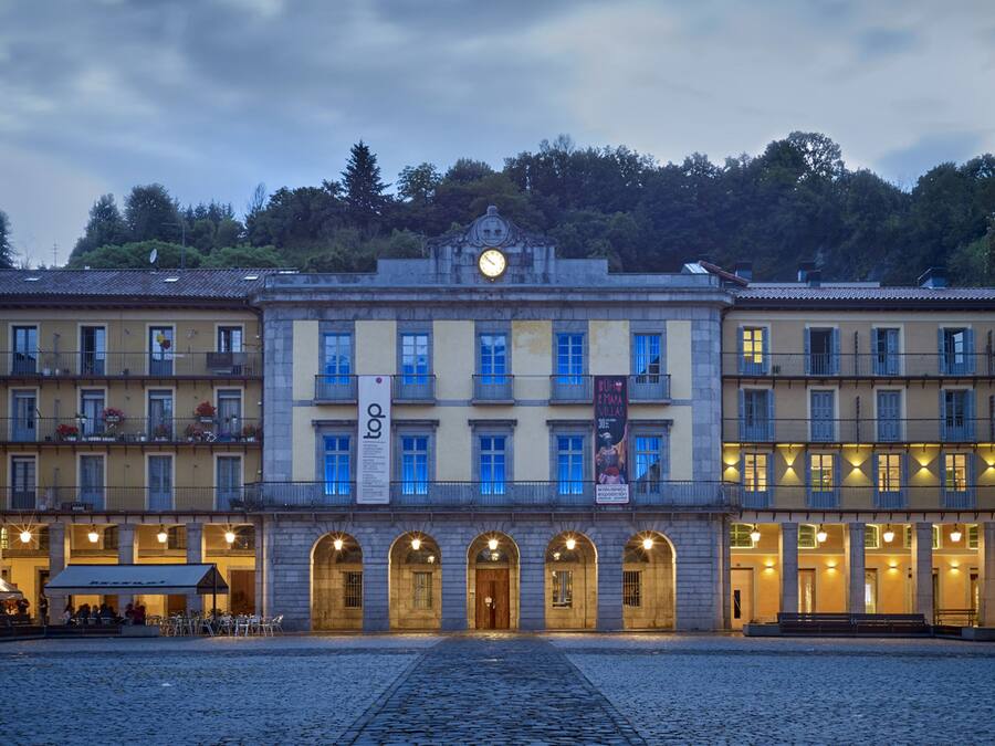 Un edificio histórico con una torre de reloj central, varios balcones y un patio empedrado.