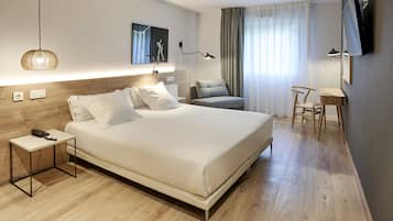 A modern hotel room with a large bed, bedside tables, a desk, a chair, and a TV mounted on the wall.