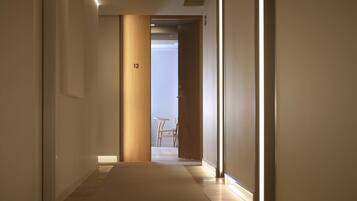 A hallway with a wooden door labeled '12', leading to a room with a small table and chair.