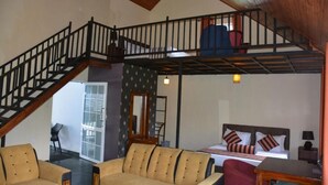 Un amplio salón con techo alto, una escalera, una cama con almohadas a rayas y un sofá.