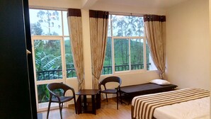 Una habitación con cama, escritorio, dos sillas y ventanas amplias con cortinas.