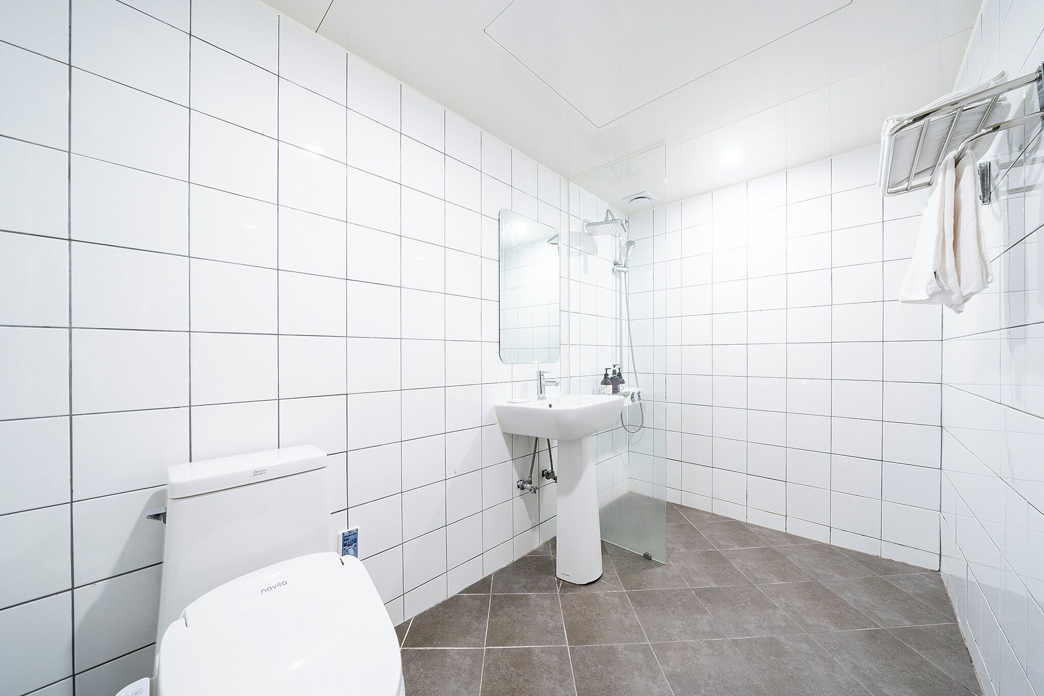 Uma casa de banho moderna com azulejos brancos, sanita branca, lavatório e chuveiro.
