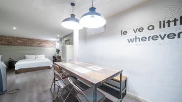 Una habitación de hotel moderna con cama, mesita de noche y escritorio con sillas. Cuenta con un equipo de aire acondicionado de pared y una lámpara de techo.