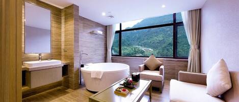 A modern bathroom with a bathtub, a large mirror, a sink, and a window offering a scenic view.