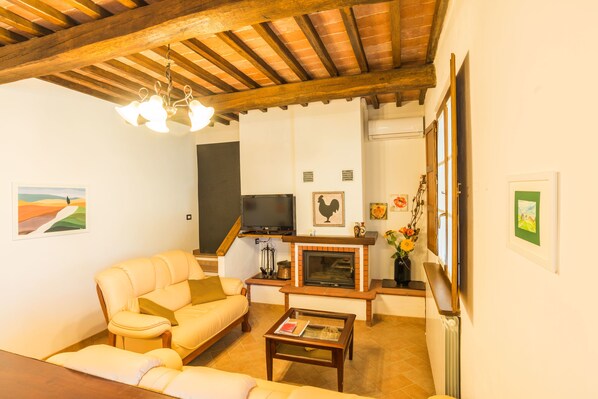 A living room with a sofa, a coffee table, a fireplace, and a television. - Agriturismo Cantagalli (San Quirico d'Orcia)