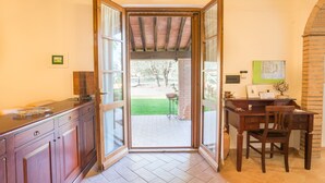 A kitchen with a wooden countertop, a dining area with a wooden table and chairs, and a view of a garden through an open door. - Agriturismo Cantagalli (San Quirico d'Orcia)