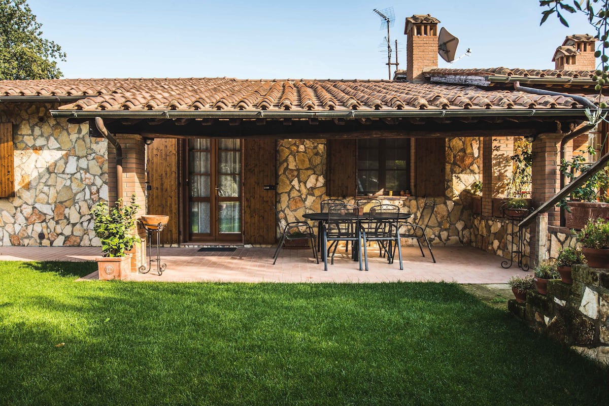 A stone building with a tiled roof, a patio with a table and chairs, and a grassy lawn.
