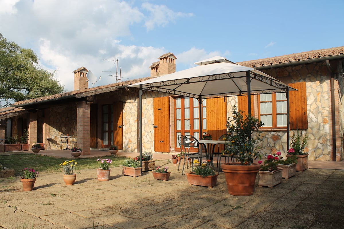 A stone building with a covered patio area, potted plants, and a table with chairs.