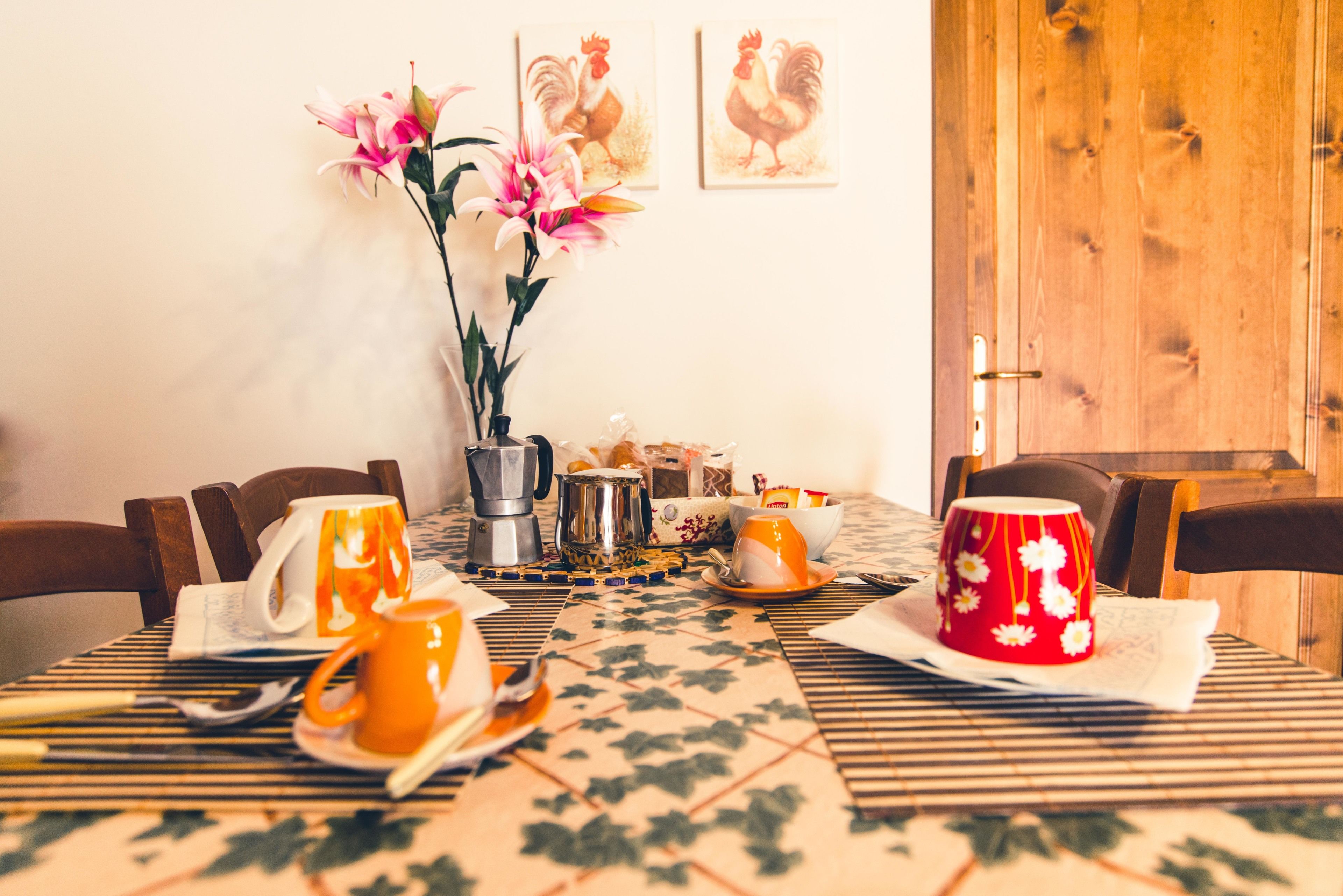 Een eettafel gedekt met verschillende gerechten, een koffiepot en een vaas met bloemen.