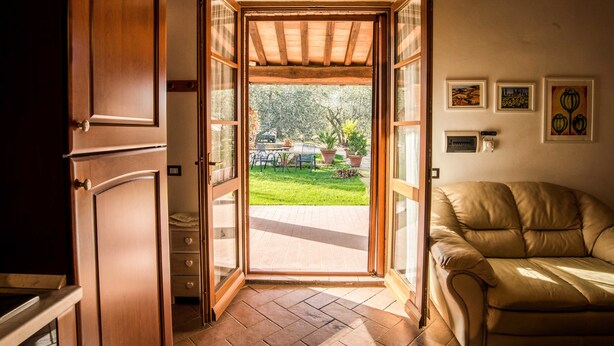 An open door leading to a patio with a lawn, a dining table, and chairs. - Agriturismo Cantagalli (San Quirico d'Orcia)