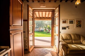 An open door leading to a patio with a lawn, a dining table, and chairs. - Agriturismo Cantagalli (San Quirico d'Orcia)