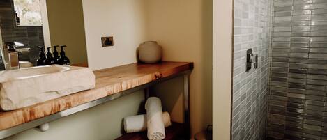 Une salle de bain avec un meuble-lavabo en bois, un miroir, un lavabo et un espace douche aux murs carrelés.