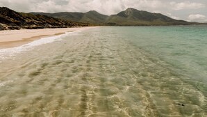 A beach with clear water, sandy shore, and mountains in the background. - Aplite House (Friendly Beaches)
