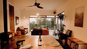 A modern dining area with a wooden table, chairs, a wine bottle, and a view of the outdoors. - Aplite House (Friendly Beaches)