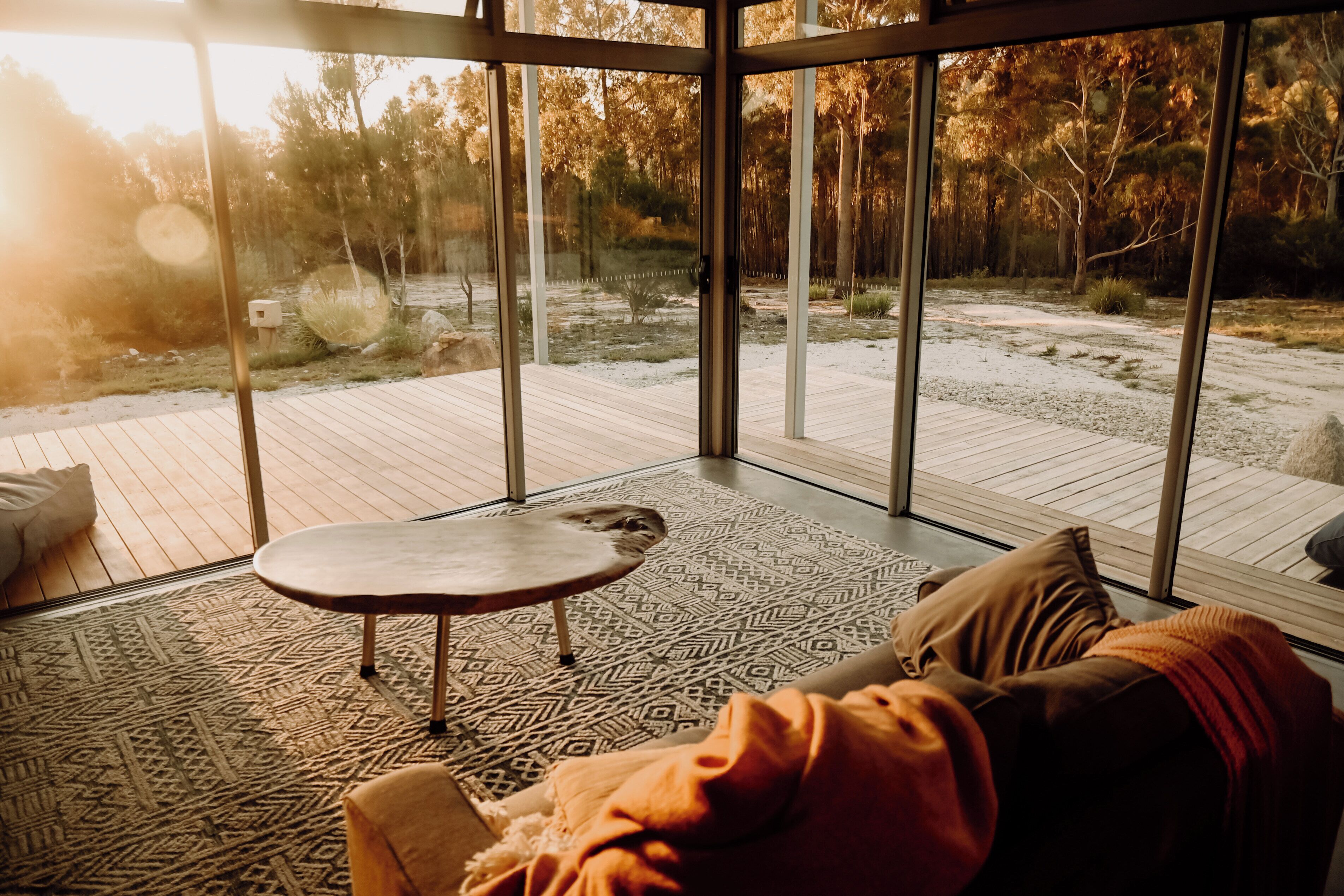 Une pièce moderne dotée d’un grand mur en verre, d’une terrasse en bois et d’un tapis à motifs.