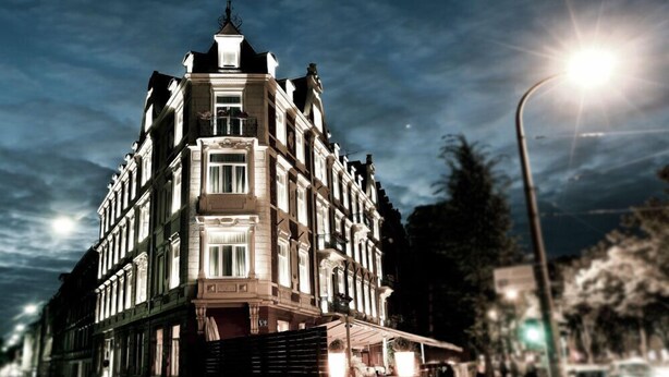 Ein historisches Gebäude mit Hauseingang an einer Ecke, großen Fenstern und einem Balkon.