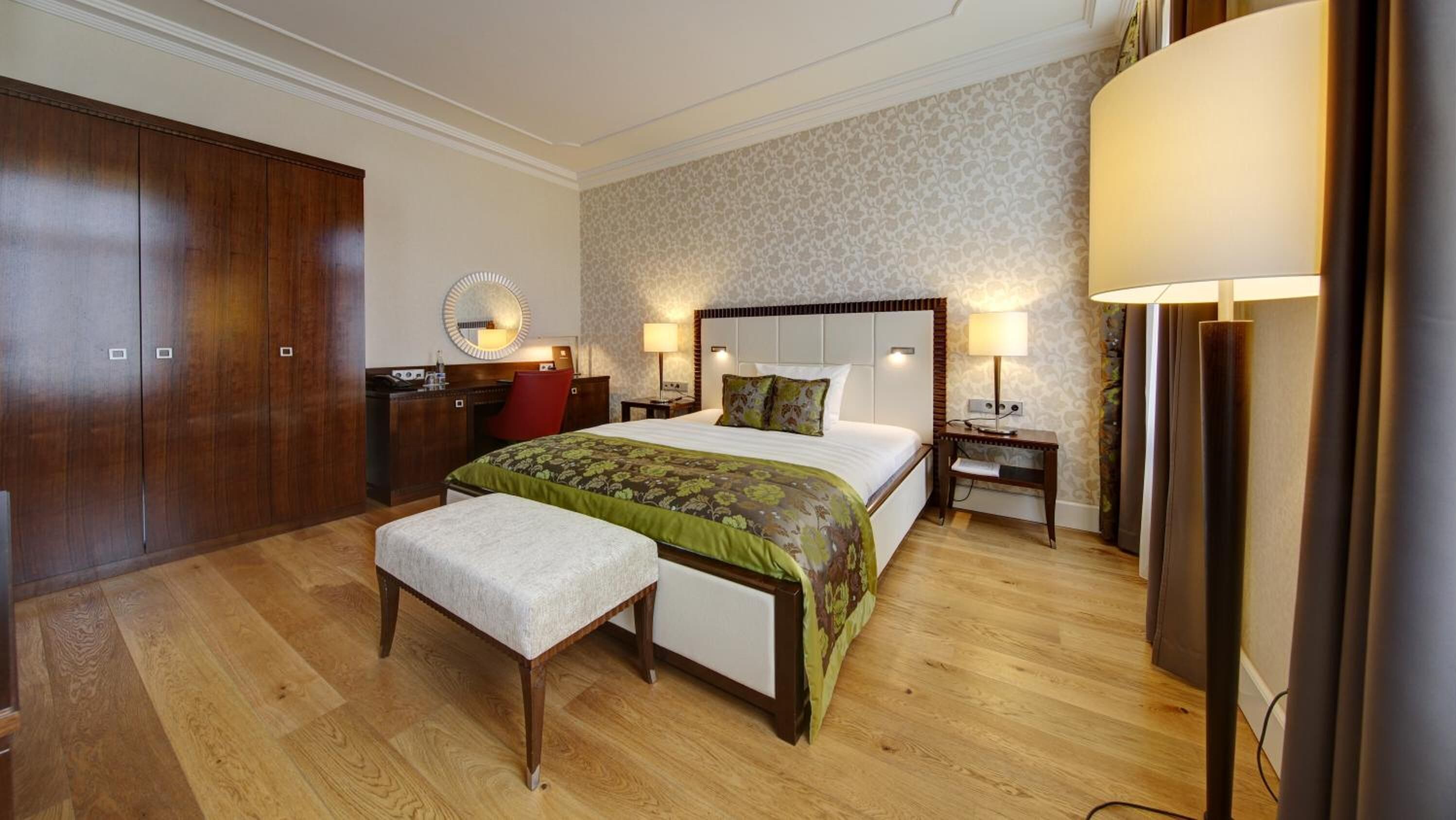 Ein Hotelzimmer mit einem großen Bett, einem Schreibtisch, einem Sessel, einem Nachttisch mit Lampen und einem Kleiderschrank.
