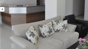 A hotel lobby with a reception desk, a sofa with floral cushions, and a coffee table with a flower vase. - Konuk Hotel (Gerede)