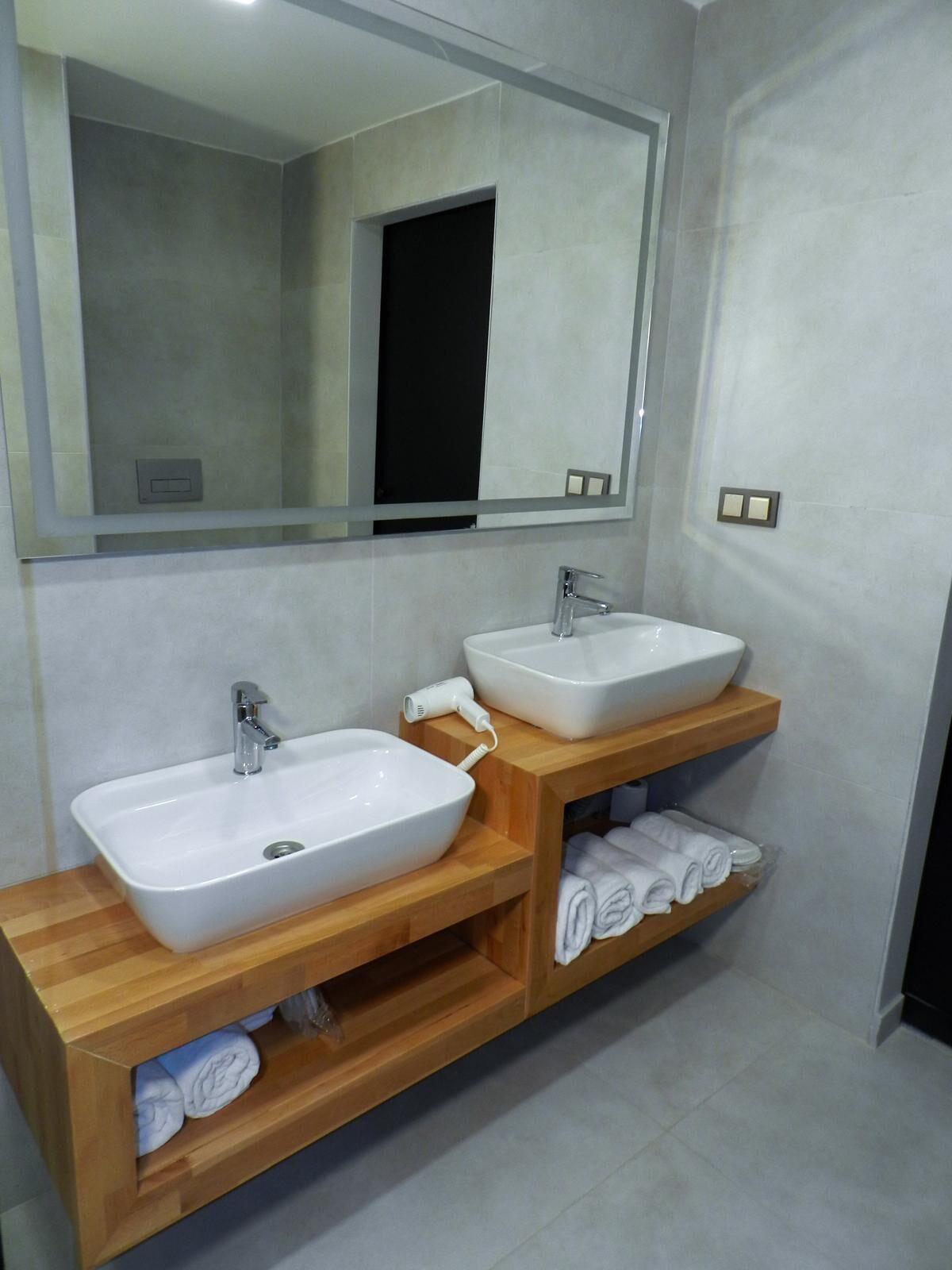 A bathroom with two sinks, a mirror, and a wooden vanity with towels.