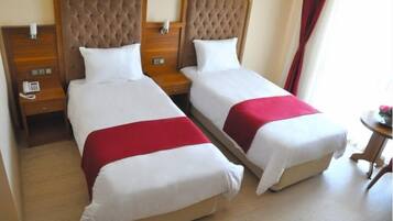 Habitación de hotel con dos camas, cada una con un cabecero capitonado y ropa de cama blanca. Mesitas de noche con teléfono y lámpara a cada lado.