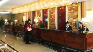 Ein Hotel-Empfangsbereich mit Marmorboden, einer Rezeption und einer großen Wanddekoration.