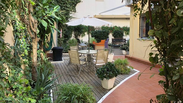 An outdoor patio area with a table and chairs, surrounded by potted plants and a wooden deck. - Hospederia Imar (Cádiz)