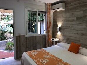 A bedroom with a bed, a small table, an air conditioning unit, and a window with a view of greenery. - Hospederia Imar (Cádiz)
