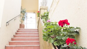 A staircase with red tiles, a wooden handrail, and potted plants with red flowers. - Hospederia Imar (Cádiz)