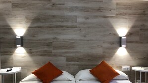 A hotel room with a modern design, featuring a large bed with white bedding and two orange pillows, two bedside tables, and wall-mounted lighting. - Hospederia Imar (Cádiz)