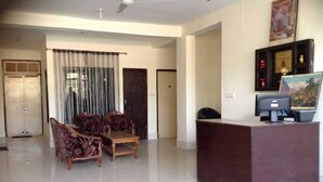 A hotel reception area with a desk, chairs, a computer, and a framed picture on the wall. - Hotel Thamsar (Palampur)
