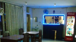 A room with a dining table and chairs, a bar area with a neon sign, and a Coca-Cola refrigerator. - Hotel Thamsar (Palampur)